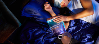 Person relaxing in bed with Sleep+ Magnesium and a mug of hot chocolate.